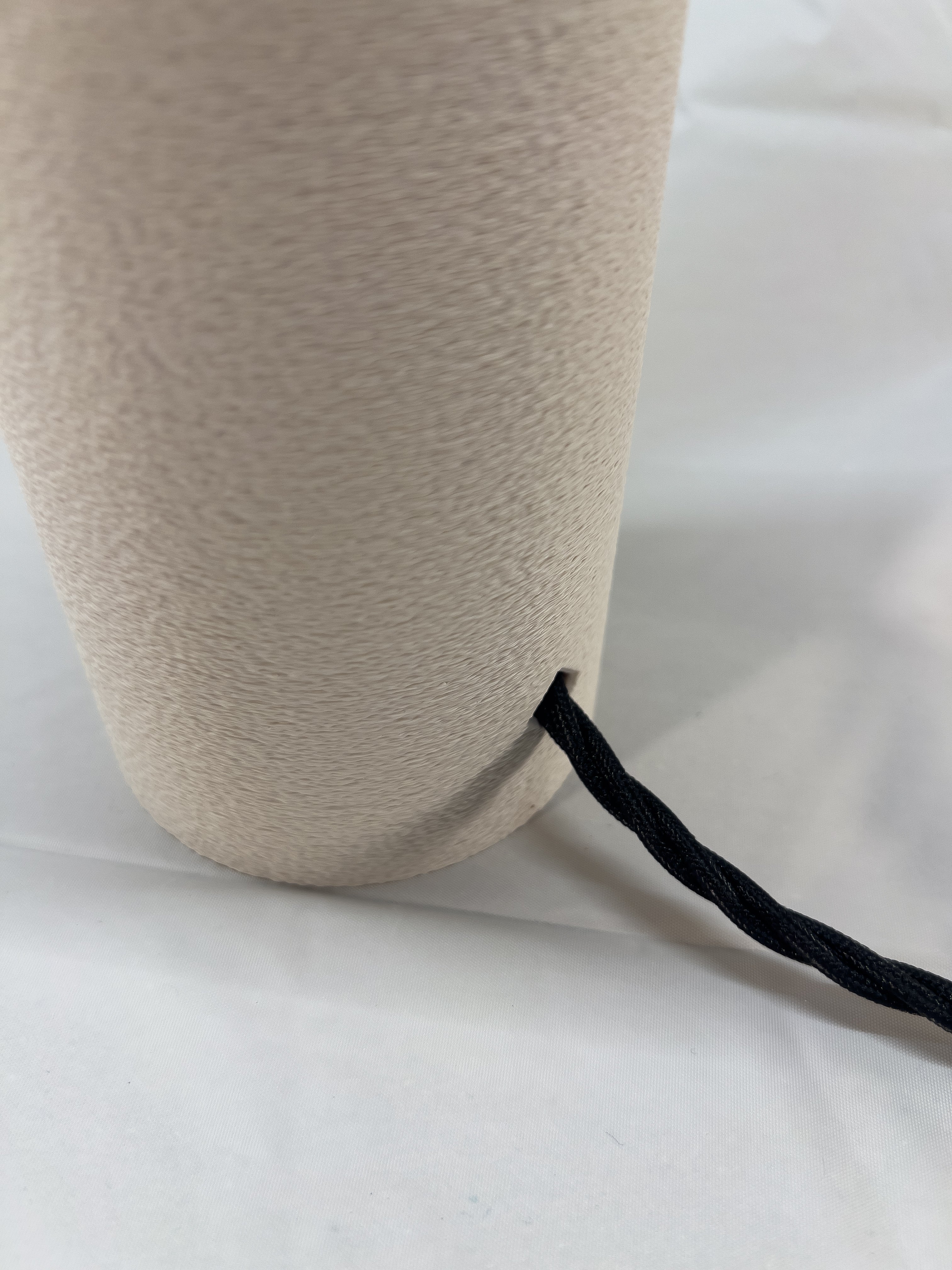 Close-up of a beige textured vase with a black cord on a white background